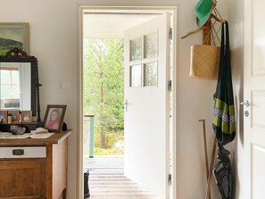 A hallway leading to an outdoor area with a wooden deck, a mirror with framed photos, and a hanging bag.
