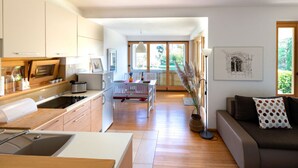 A modern kitchen with wooden cabinets, a dining area with a white table and chairs, and a living room with a sofa and a floor lamp. - Apartment Casa Bamboo (Medulin)