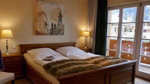 Ein Hotelzimmer mit einem hölzernen Bett, zwei Nachttischlampen, einem Stadtplakat und einem Balkon mit Blick.