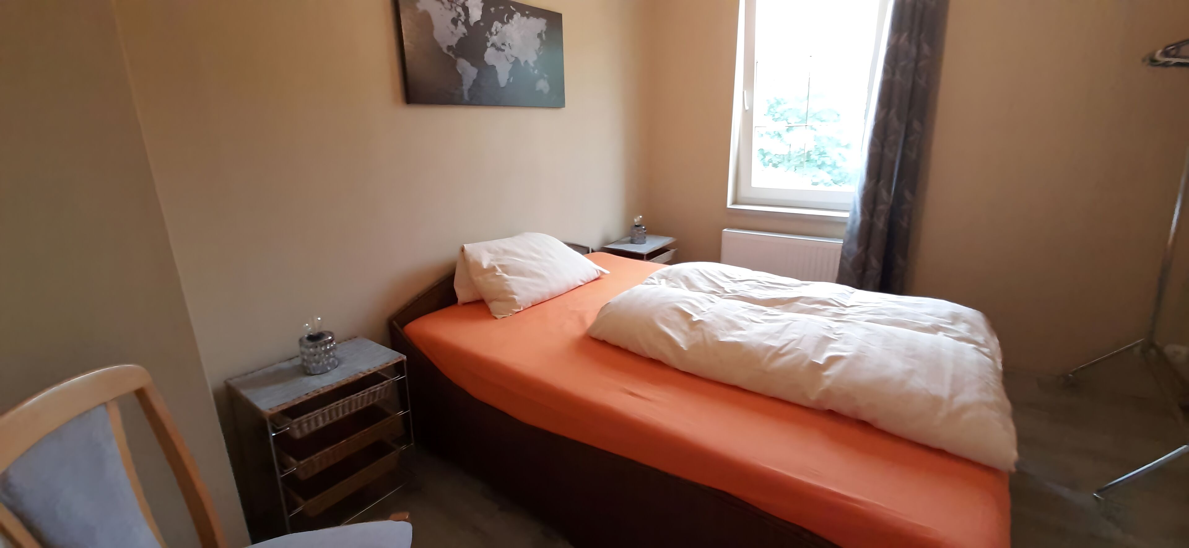 A bedroom with a bed, a nightstand, a chair, a small table, and a window with curtains.