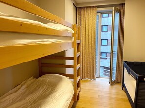 Ein Zimmer mit zwei Etagenbetten, einer schwarzen Schlafcouch und einem Fenster mit gemusterten Vorhängen.