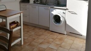 Ett kompakt kök med tvättmaskin, mikrovågsugn och kaffebryggare.