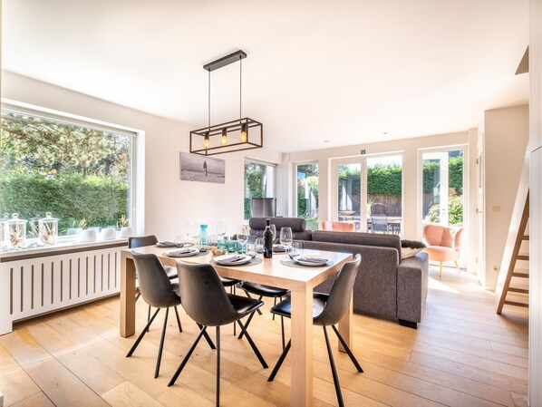 Uma ampla sala de jantar com uma mesa grande, cadeiras modernas e vista para o exterior.