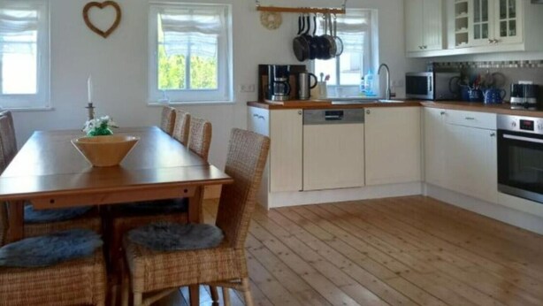A modern kitchen with white cabinets, a wooden dining table, wicker chairs, and a heart-shaped decoration on the wall. - Vincent Family Holiday Home (Bertsdorf-Hoernitz)