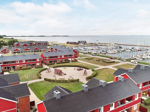 A coastal residential area with red brick buildings, a marina with boats, and a central playground. - 4 Person Holiday Home on a Holiday Park in Lemvig (Lemvig)