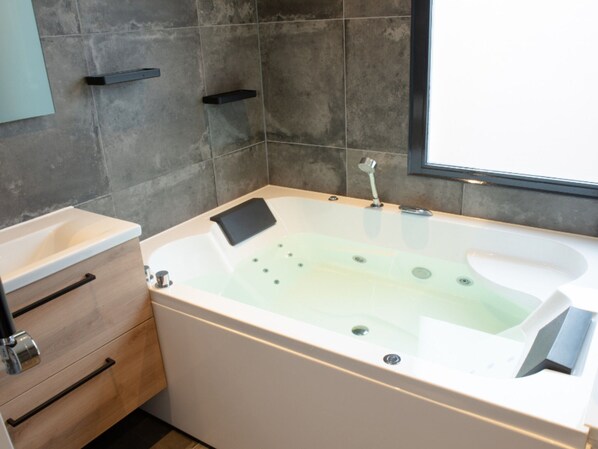 Une salle de bain moderne avec une baignoire sur pieds, un meuble en bois doté de tiroirs et une grande fenêtre laissant entrer la lumière naturelle.