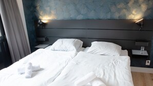 A double bed with white linens and towels, a dark headboard, and a patterned wall. - Holiday Home in Zevenhuizen With Sauna (Zevenhuizen)