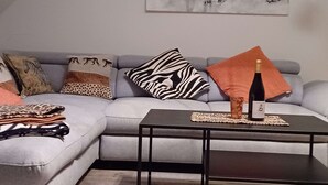 A modern living room with a grey sofa, patterned cushions, a black coffee table, and a wine bottle. - Holiday Apartment Monet in Oberrotweil (Vogtsburg)