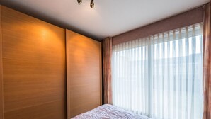A hotel room with a large bed, wooden panel walls, and a large window with sheer curtains. - Apartment With 2 Bedrooms and Large Terrace (Middelkerke)