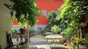 Un espace extérieur aménagé en terrasse, avec une table et des chaises, entouré de plantes en pot et d’un mur rouge.