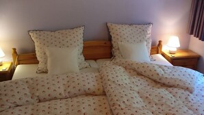A bed with a floral-patterned duvet, two pillows, and a wooden headboard. There are two bedside tables with lamps. - Ahlers Holiday Apartment (Schneverdingen)