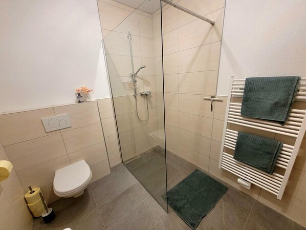 A modern bathroom with a glass shower enclosure, a toilet, a towel rack with two towels, and a small plant on the wall. - New Apartment in the Beautiful Pitztal (Sankt Leonhard im Pitztal)