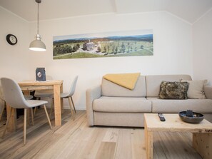 A modern living room with a sofa, a coffee table, and a dining area with chairs and a table. A painting of a landscape is on the wall. - Ferienwohnung im Sauerland Nahe der Skipiste (Winterberg)