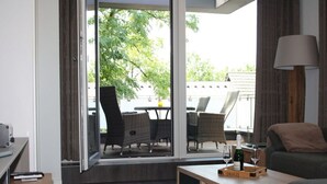 A modern living room with a sofa, a coffee table, and a dining area visible through a glass door.