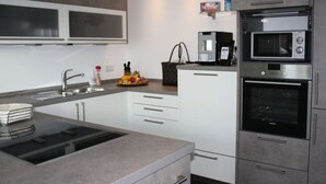 A modern kitchen with a built-in stove, microwave, and oven. There is a sink with a faucet, a countertop with a fruit bowl, and a coffee maker.