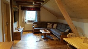 Une pièce mansardée chaleureuse avec un plafond en bois, un canapé, une table et une fenêtre avec des rideaux.