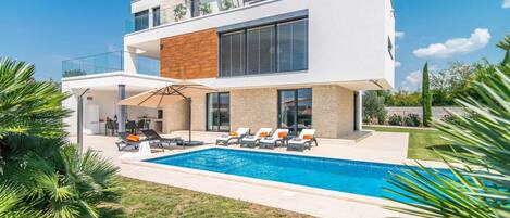 Uma casa moderna de dois andares com piscina, área de estar externa e um jardim bem cuidado.
