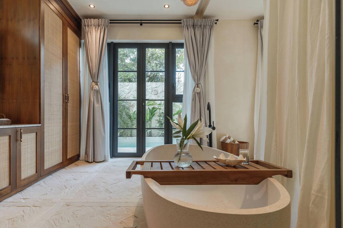 A bathroom with a bathtub, a wooden vanity, and a large window with curtains.