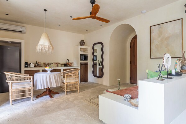 A modern kitchen with a dining area, featuring a ceiling fan, white cabinetry, and a dining table with chairs. - The Revery Bali (Canggu)