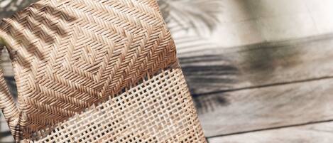 Una silla de mimbre con respaldo trenzado y un cojín oscuro de estampado geométrico.