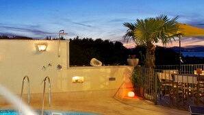 Piscina com vista para o pôr do sol, uma palmeira e área de estar externa.