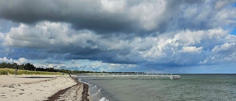 A beach with a sandy shore, a pier extending into the water, and a cloudy sky.