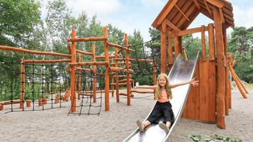 Un parque infantil con tobogán, estructuras para escalar y una casita de madera.