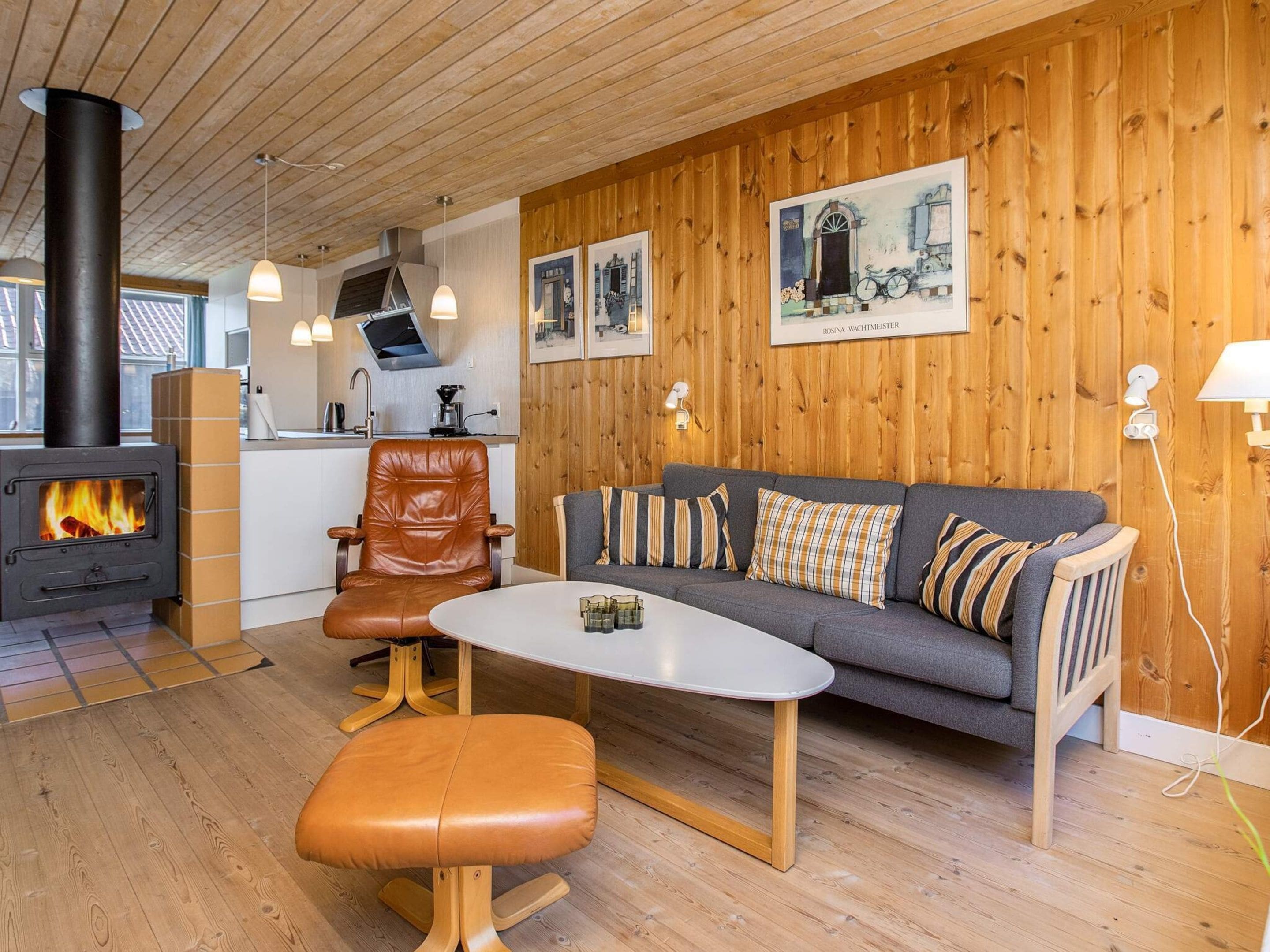 Una sala de estar acogedora con un sofá, una mesita de centro y un sillón de cuero. Se aprecia una chimenea al fondo.