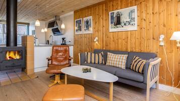 Una sala de estar acogedora con un sofá, una mesita de centro y un sillón de cuero. Se aprecia una chimenea al fondo.