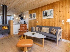 Una sala de estar acogedora con un sofá, una mesita de centro y un sillón de cuero. Se aprecia una chimenea al fondo.