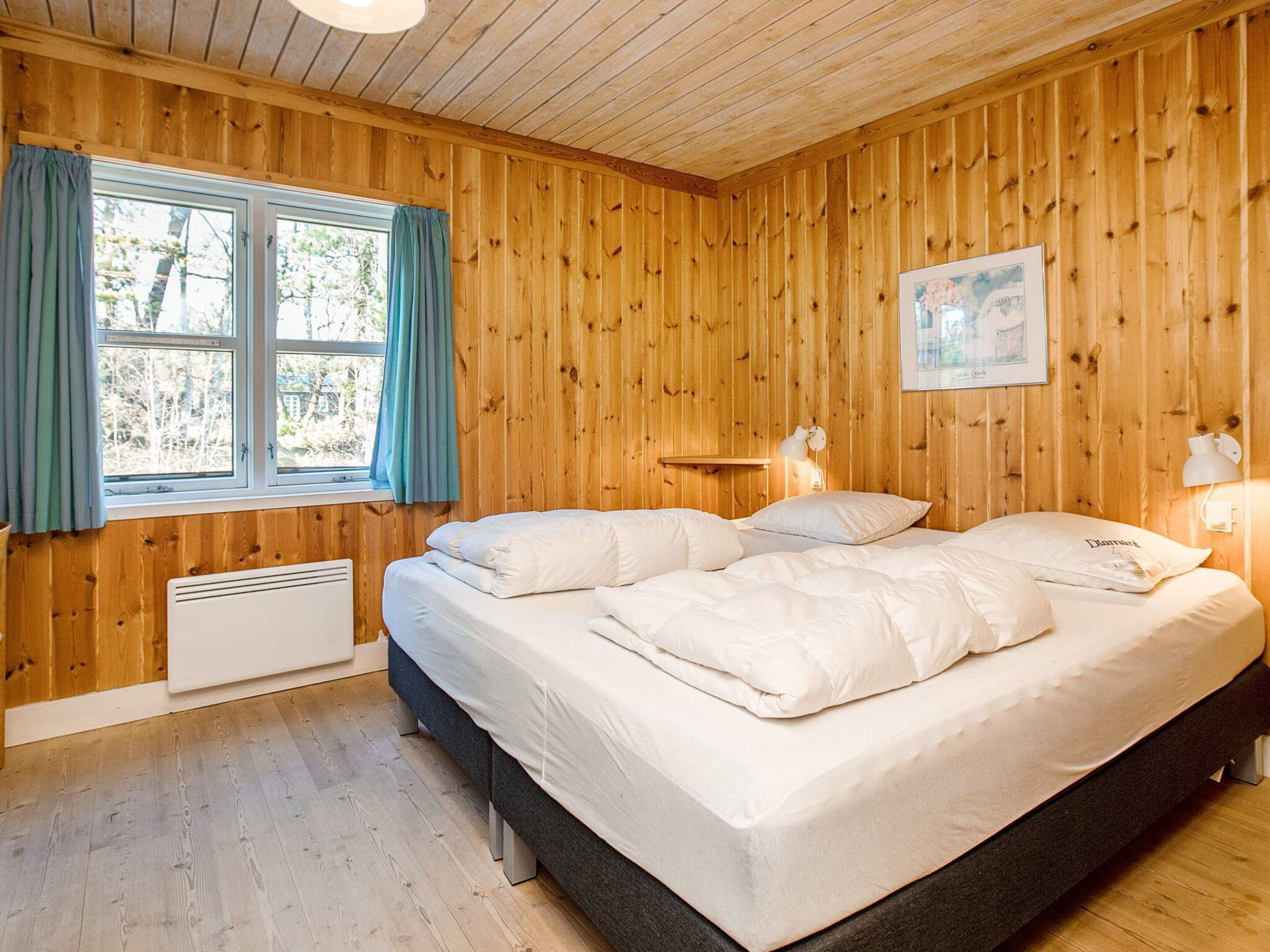 Ein Schlafzimmer mit Holzvertäfelung, einem Bett, zwei Nachttischlampen, einem Fenster mit Vorhängen und einem Heizkörper.