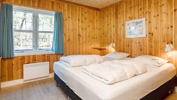 Ein Schlafzimmer mit Holzvertäfelung, einem Bett, zwei Nachttischlampen, einem Fenster mit Vorhängen und einem Heizkörper.