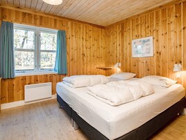 Un dormitorio con paneles de madera, una cama, dos lámparas de noche, una ventana con cortinas y un radiador.