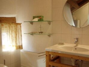 A bathroom with a white sink, wooden vanity, and two glass shelves with toiletries. - "zum Kirchenschuster" (Schernfeld)