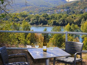 A table with two wine glasses and a bottle, overlooking a river and forested hills. - Holiday Apartment Schlossberg (Lorch)