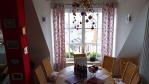 A dining area with a round table, six chairs, and a window with floral curtains. - Holiday Apartment Wedel (Augsburg)