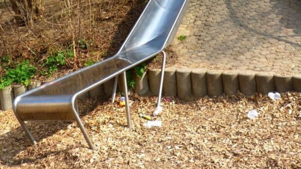 A metal slide in a park with a paved path and trees in the background. - Holiday Apartment Wedel (Augsburg)