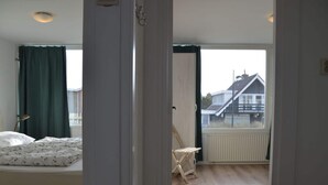 A bedroom with a bed, a radiator, a window with curtains, and a view of a house outside.