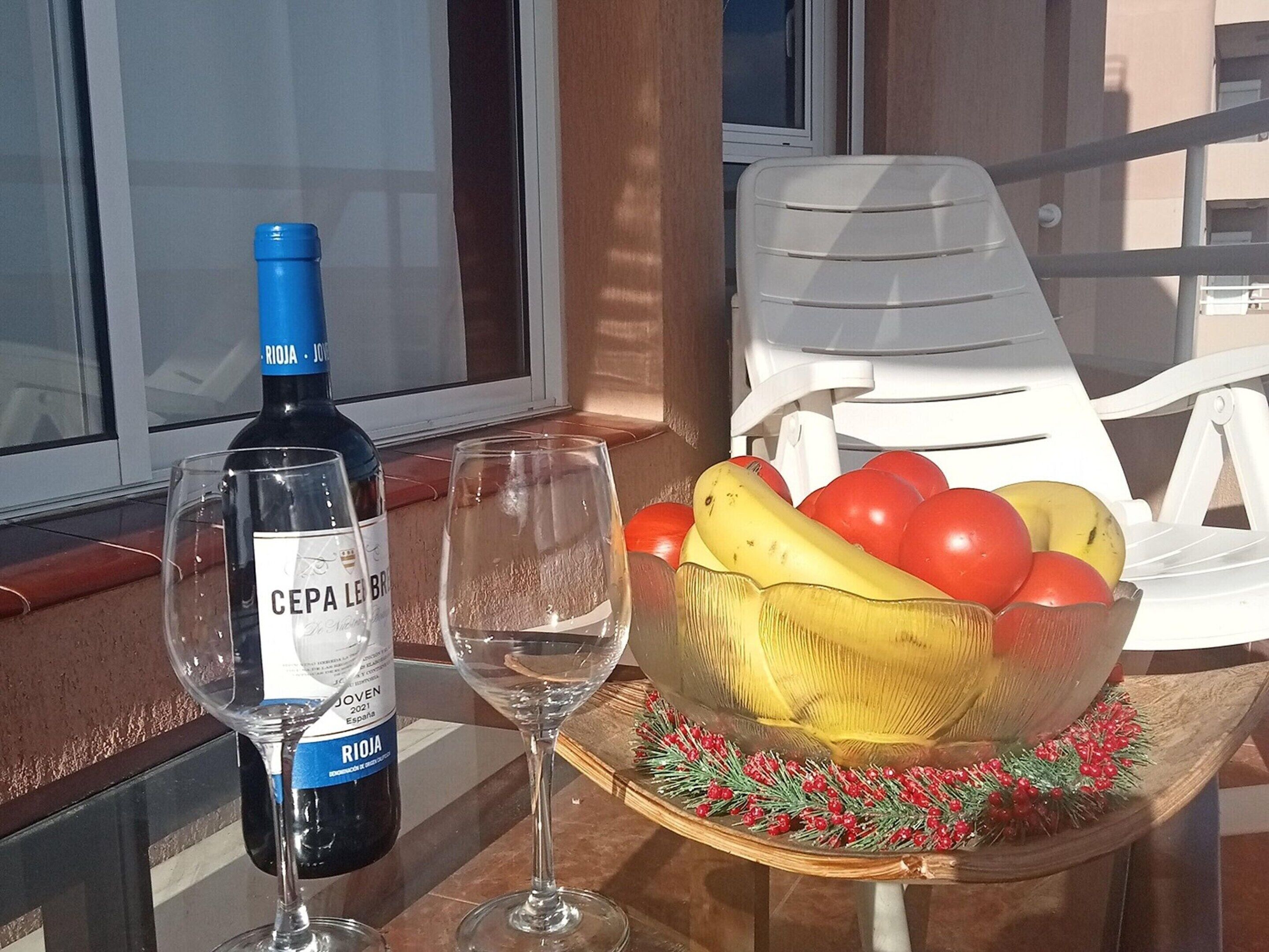 A table with a bottle of Rioja wine, two glasses, and a bowl of fruit on a balcony.