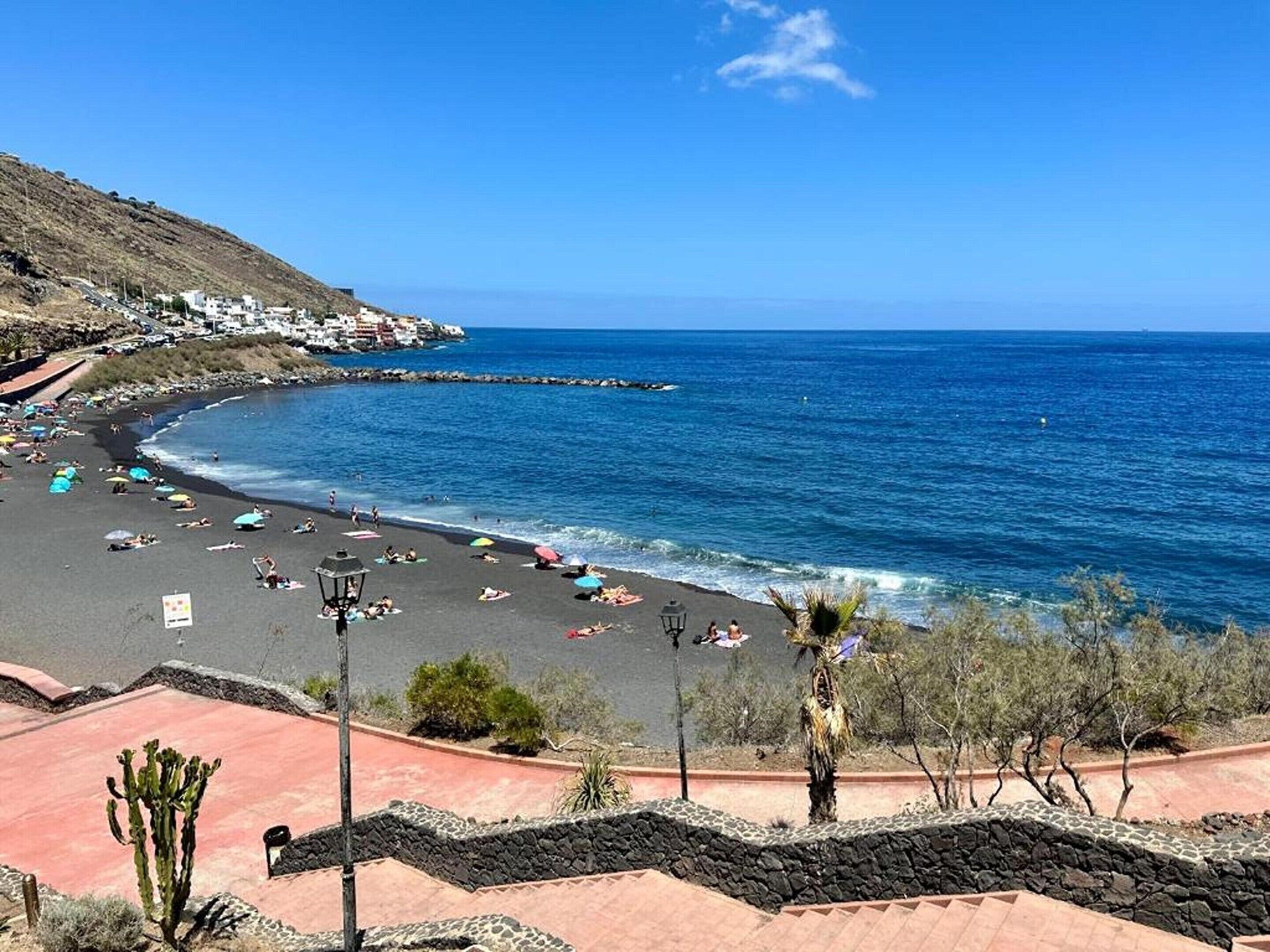 A beach with a curved shoreline, a clear blue sky, and a few umbrellas.