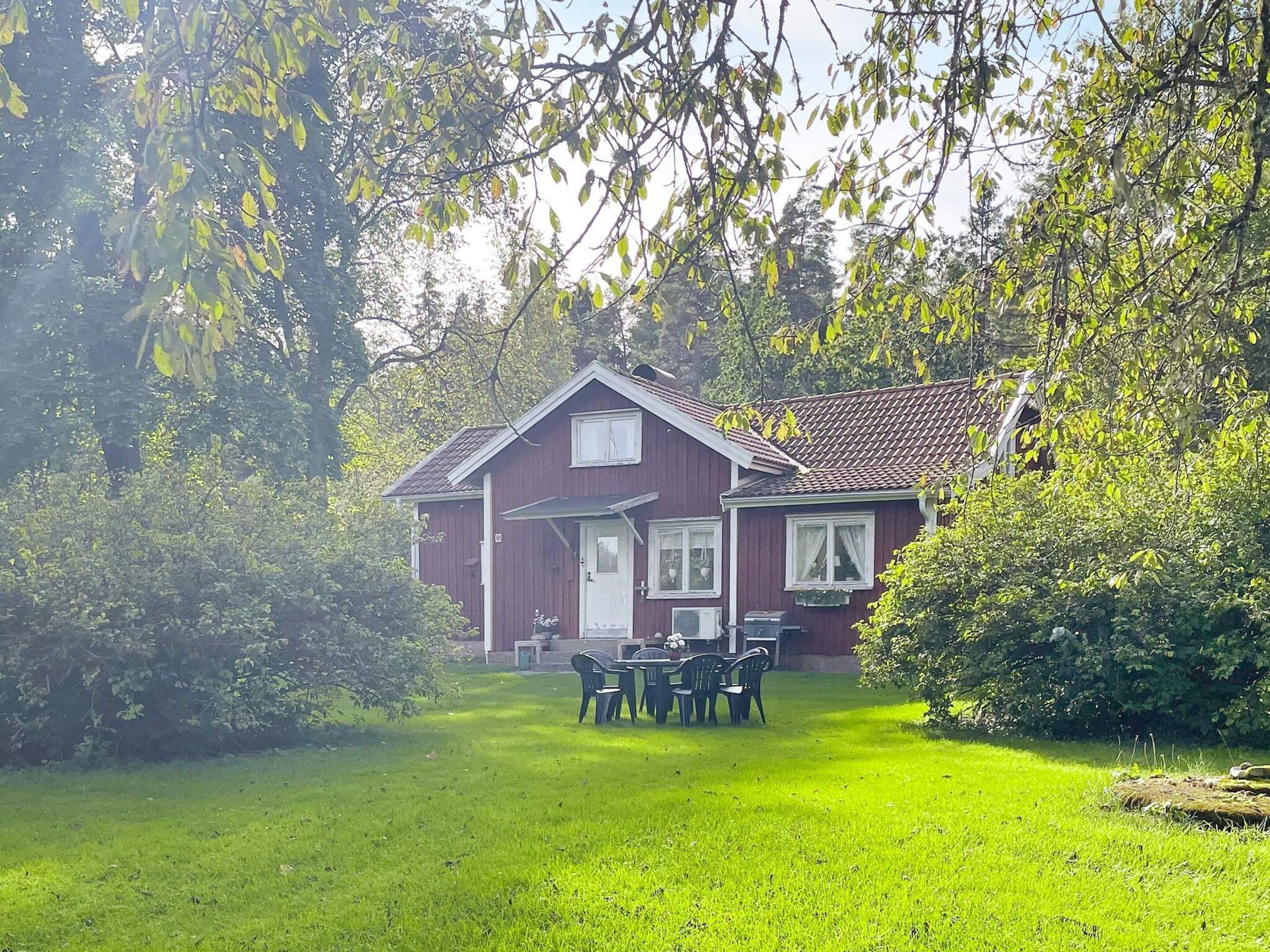 A red house with a white door and windows, surrounded by green grass and trees.