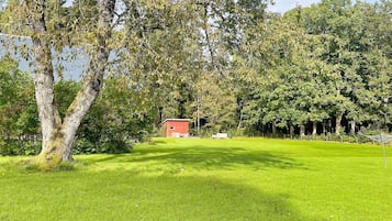 A grassy field with a red building and trees in the background.