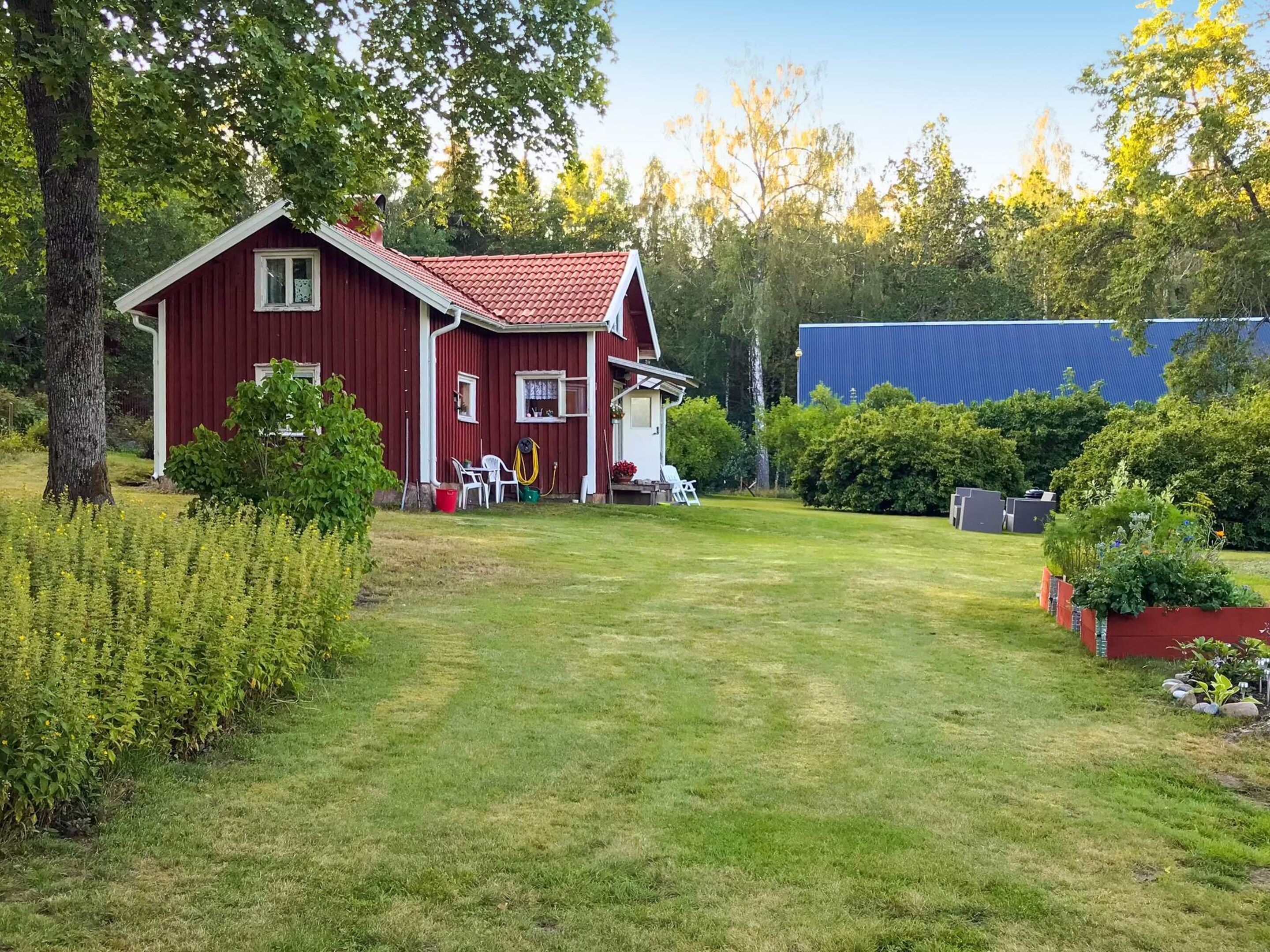 A red house with a sloped roof, surrounded by a well-maintained lawn and various plants.