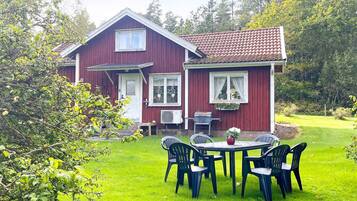 A red house with a tiled roof, a front porch, and a dining area with plastic chairs and a table.