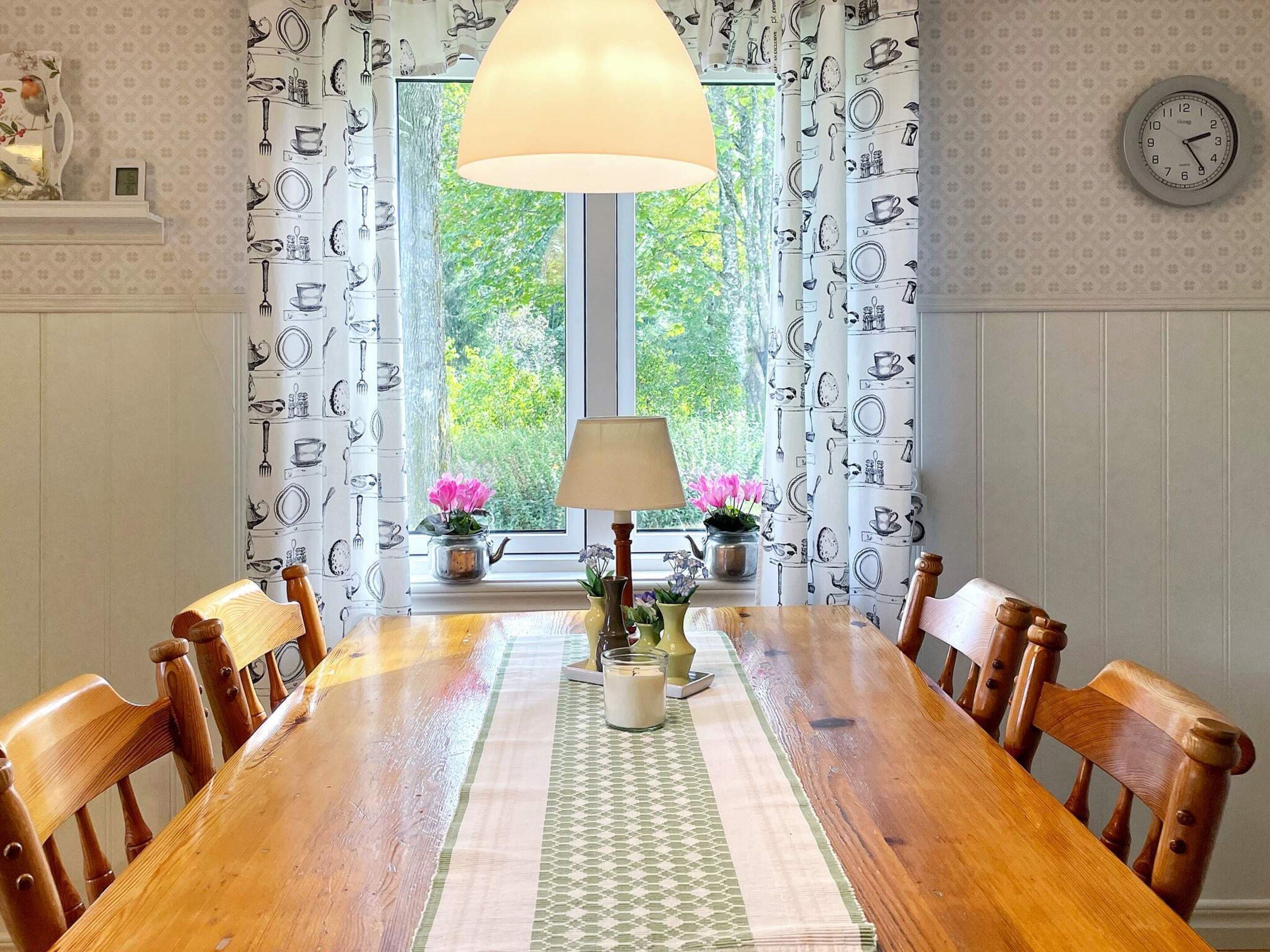 Une salle à manger avec une table en bois, des chaises, une lampe et une fenêtre avec des rideaux.