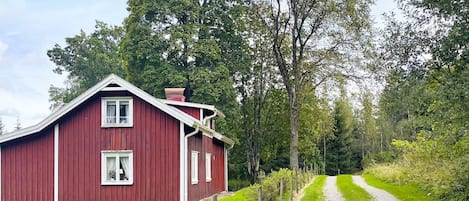 A red barn with a white window, surrounded by lush greenery and a gravel path.