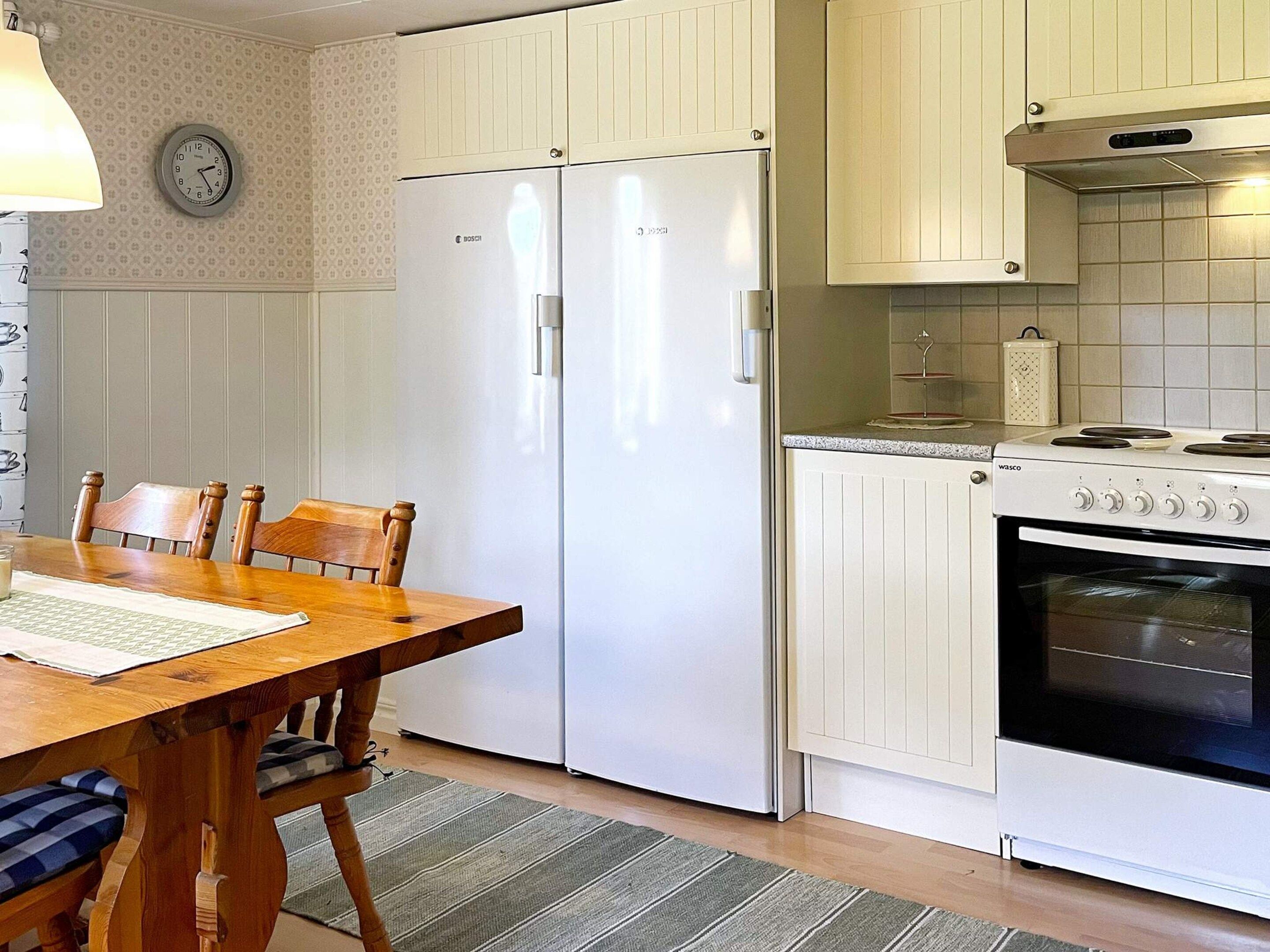A kitchen with a wooden dining table, chairs, a white Bosch refrigerator, a Wasco stove, and a clock on the wall.