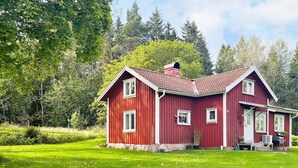 Una casa vermella de fusta amb un teulat inclinat, envoltada d'un jardí ben cuidat i arbres frondosos.