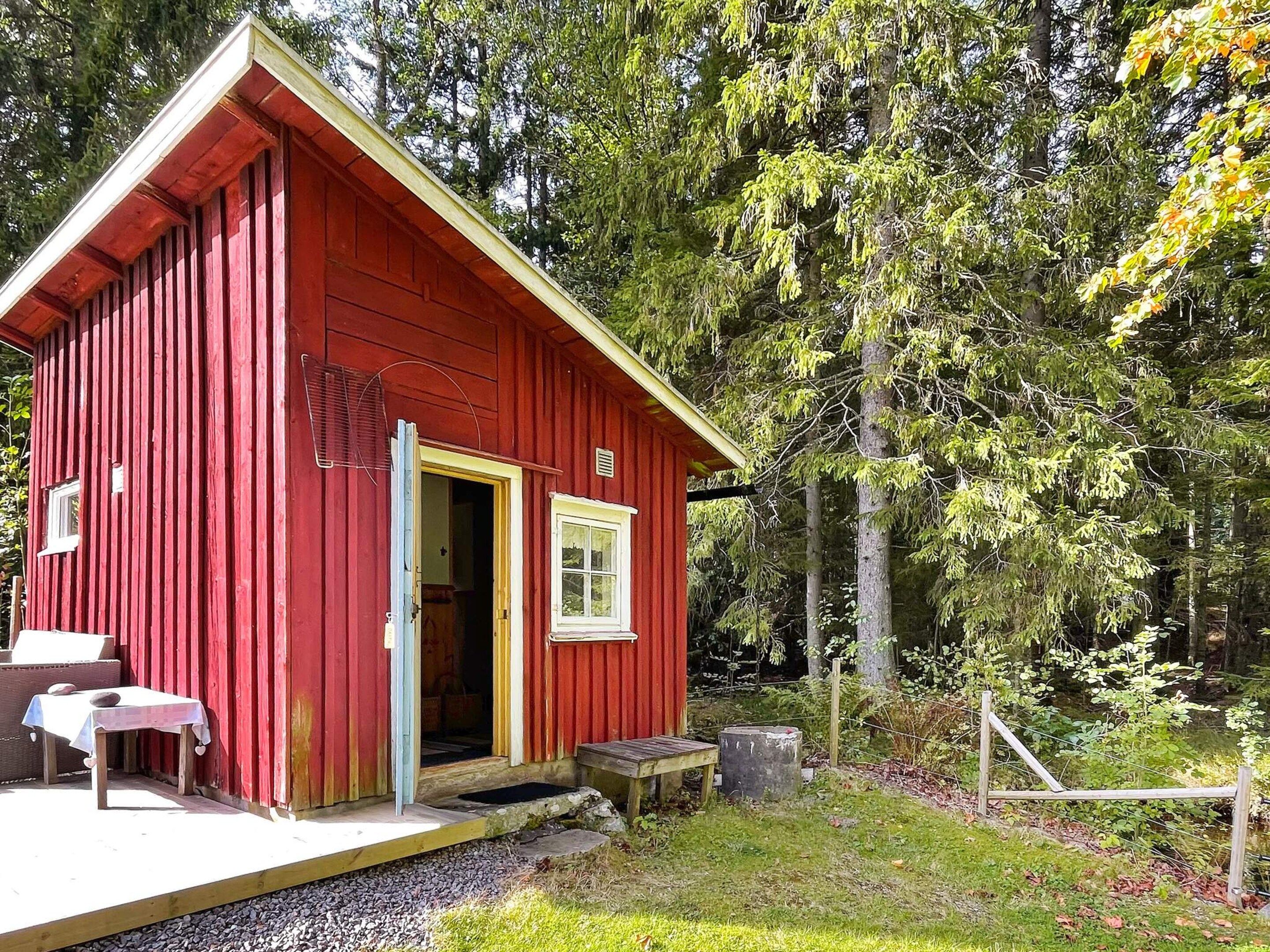 A red wooden cabin with a door open, a small table outside, and a bench.