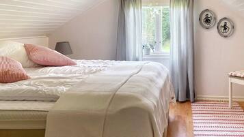 A bedroom with a sloped ceiling, a bed with white bedding, striped curtains, and a small table with a lamp.